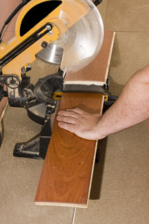 Man’s hand cutting a hardwood plank using a power miter.