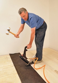 Man using a dead-blow hammer on a pneumatic nailer for hardwood flooring.