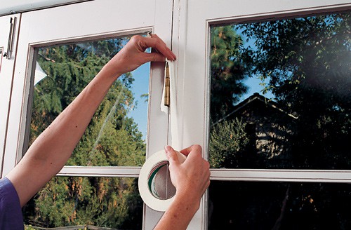 Woman's hands covering a window hinge using a masking tape.