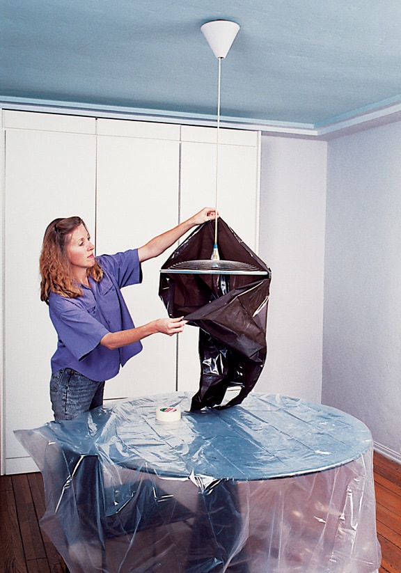 Woman covering a pendant light with a garbage bag.
