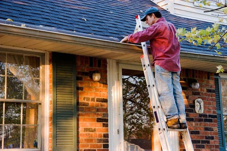 Man working on a house's rain gutter using a step ladder.