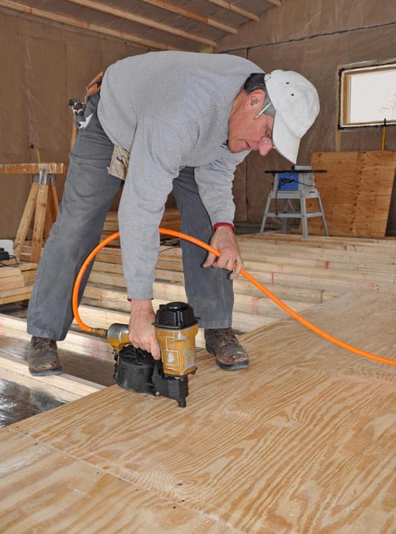 A man securing plywood as subflooring using an electric nail gun.