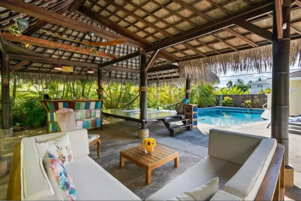 A thatched patio roof evokes a tropical paradise in this expansive backyard oasis, complete with a pool and inviting lounge area.