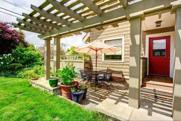 A wooden pergola frames this inviting backyard space, where metal furniture and a red door create a striking contrast against the lush greenery.