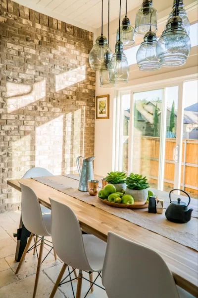 This dining area blends rustic brick and a natural wood table with modern chairs and lighting.