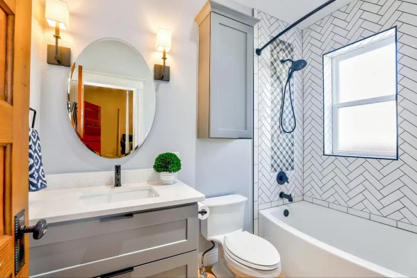 Herringbone tile pattern and sconce lights that flank an oval mirror punch-up the design of this small bathroom.