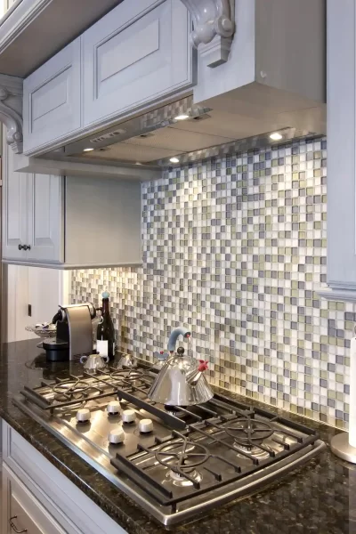 Mosaic tiles in backsplash add some texture and vibrancy amid plain white cabinets.