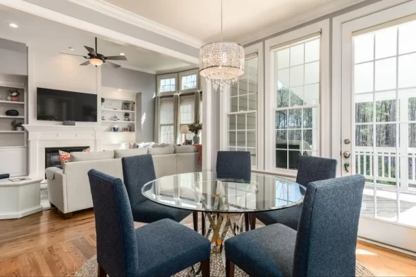 Round glass table with an overhead chandelier creates the dining area in this home.