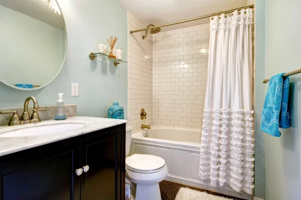 Frilly curtains, round mirror, white tiles and dark brown cabinet give this small bathroom plenty of visual interest.