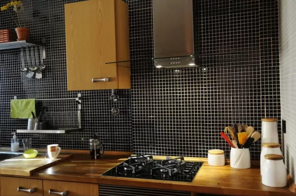 A primarily black tile backsplash combines with wooden cabinets and countertops to create a kitchen that is stylish and warm.