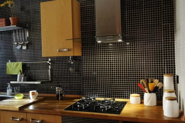 Black mosaic tiles in the backsplash add sophistication to the kitchen and complements wooden elements.