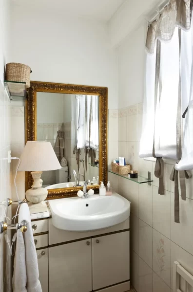 Sheer curtain with frills and metallic mirror frame elevates the beauty of this small bathroom.