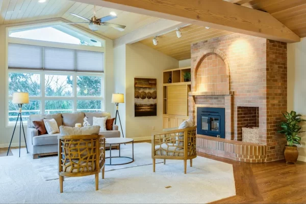 The majestic brick fireplace commands attention as a natural accent wall, grounding this airy living room with its warmth and texture.